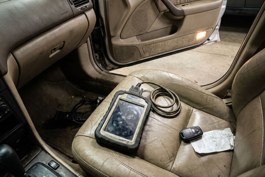 A handheld key programming device connected to a car's diagnostic port with a proximity fob on the seat